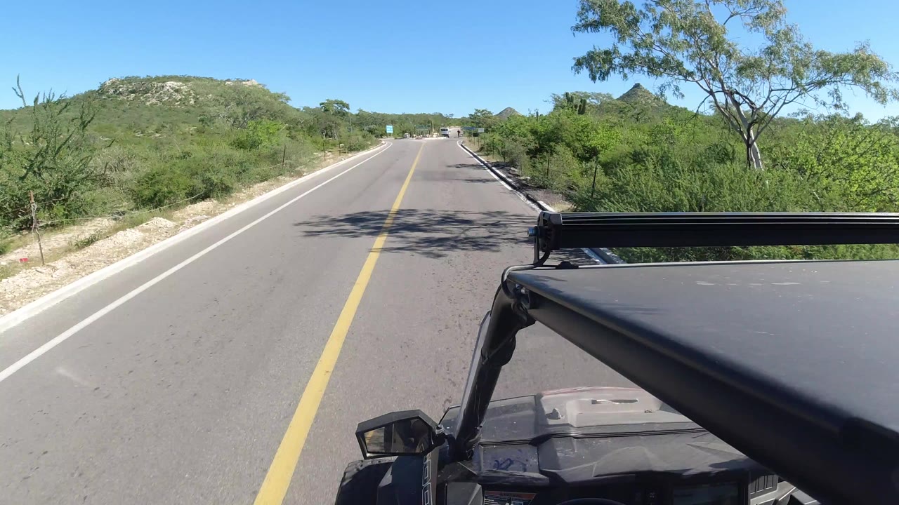 Forward road view from an open vehicle in dry green brushland.