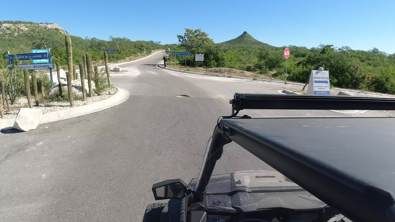 Vehicle roof view at a road junction with signs and desert greenery.
