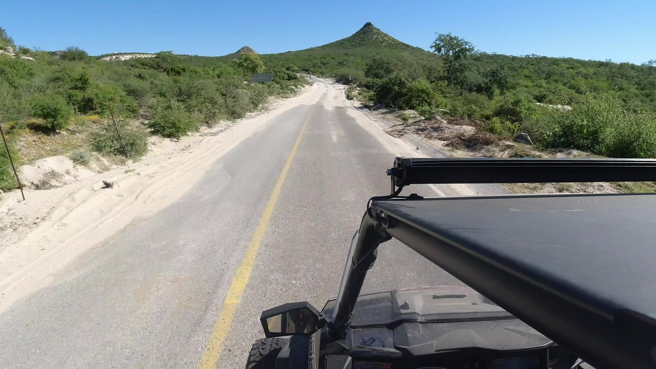 Sandy road ahead with jeep roof visible and green hills beyond.