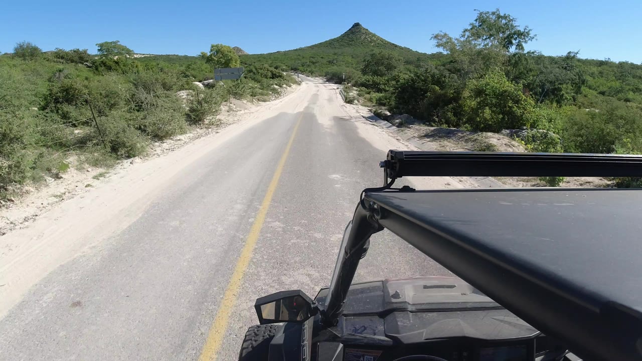 Sandy road curves through brush with jeep roof at right.