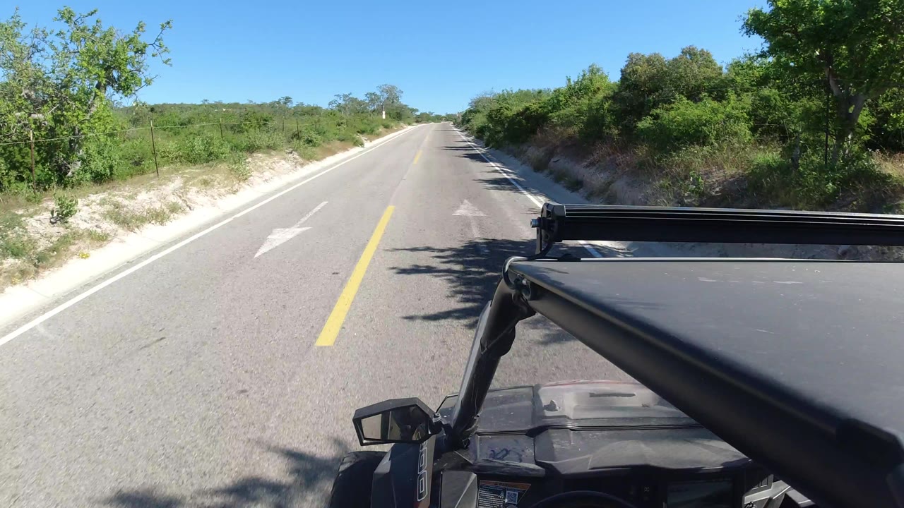 The Los Cabos road continues straight ahead, with the black truck roof and roll bar occupying the lower right foreground and no visible people in frame.