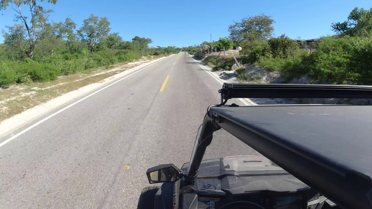 Empty paved road with scrub vegetation and vehicle roof bar in the foreground.