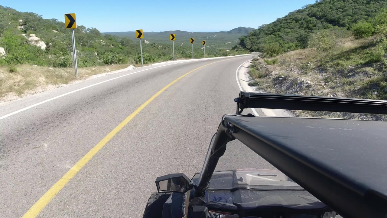Moving vehicle viewpoint on a curving mountain road with warning signs.