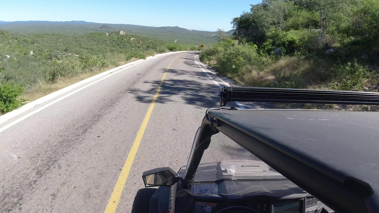 Rural road curving past brush and hillside from an ATV view.