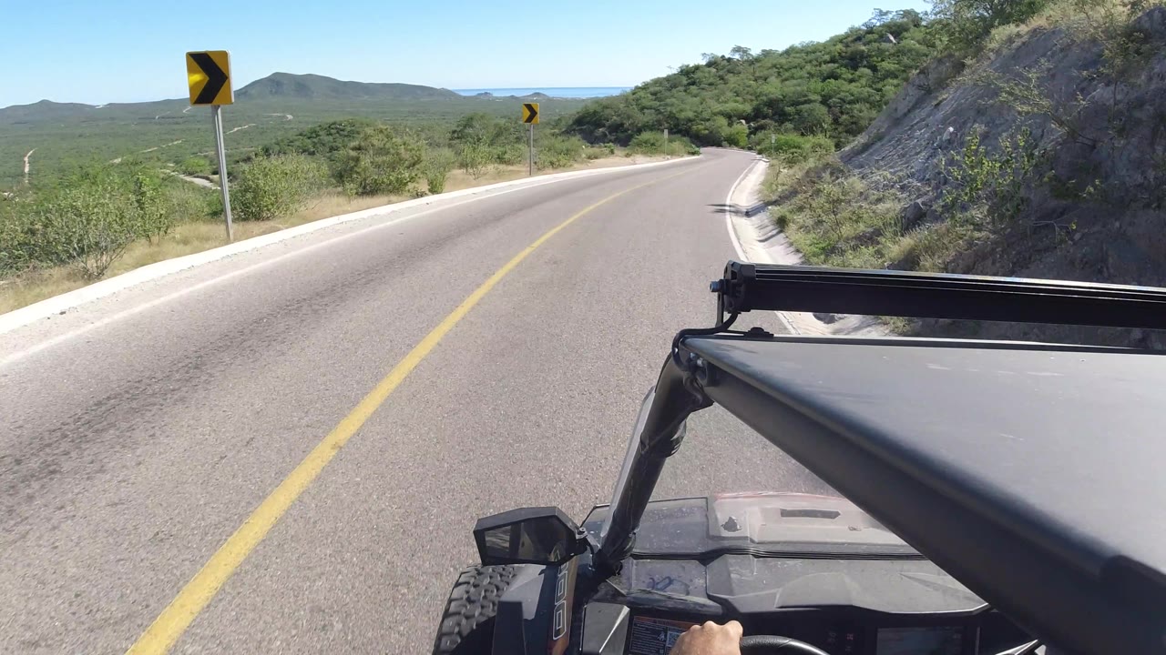 Road bending right beside a rocky hillside and roadside greenery.