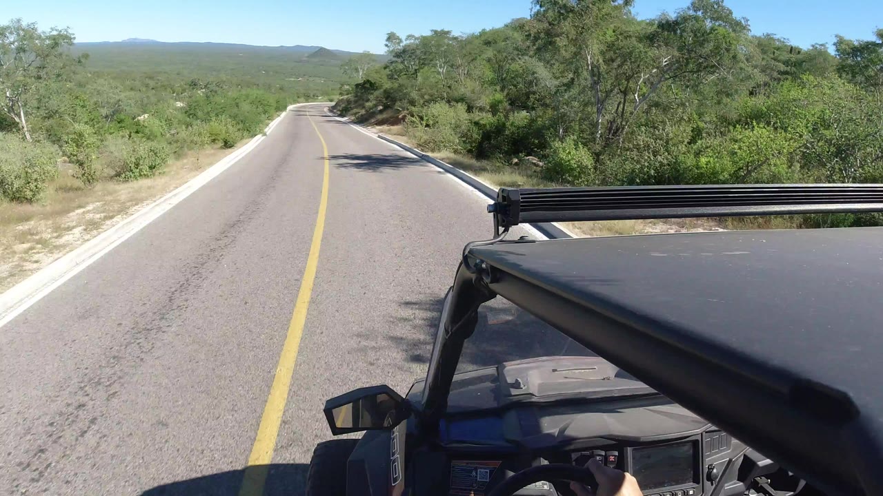 Forward view from an off-road vehicle on a paved road through green hills