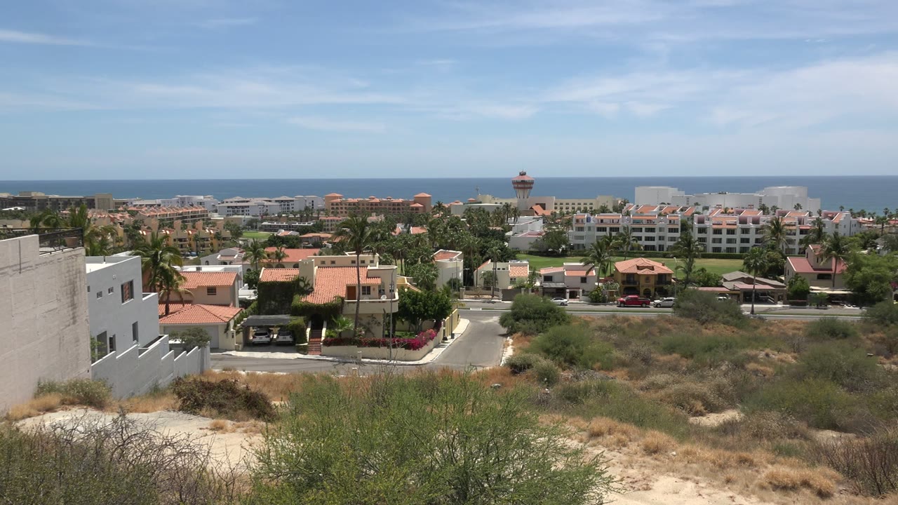Coastal town seen over dry scrub with ocean beyond.