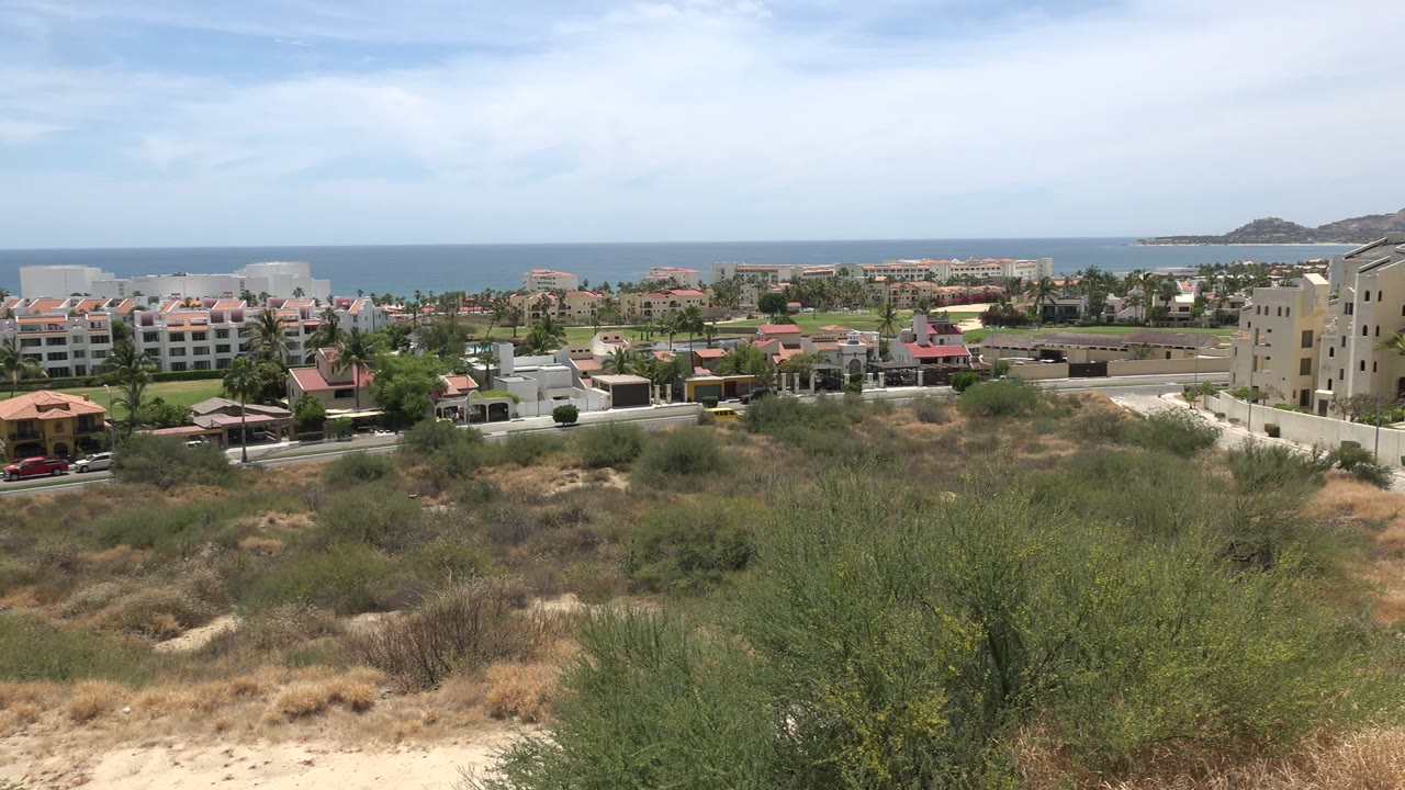 Dry scrubland overlooking coastal homes and the ocean.
