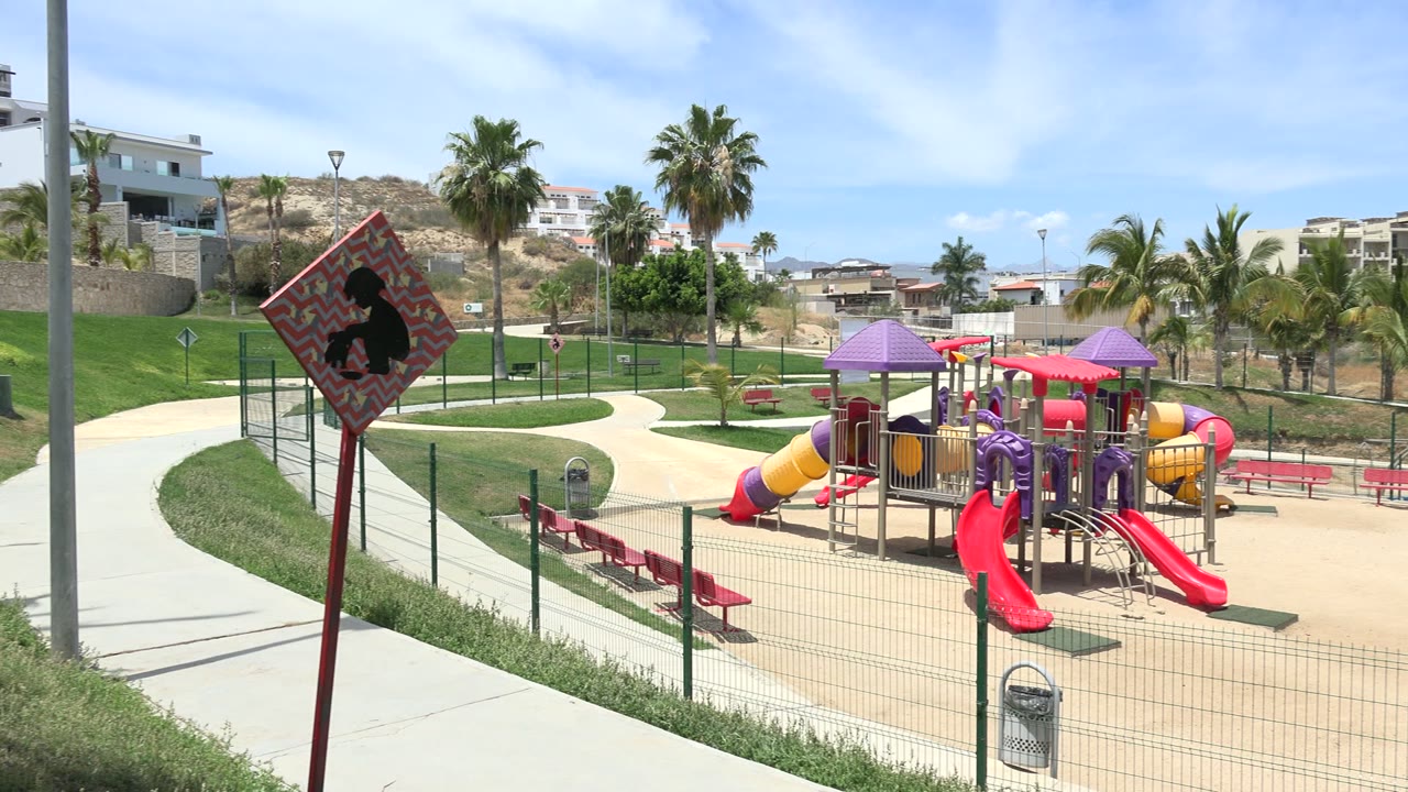 Second frame shows the Los Cabos playground centered behind a fence, with red slides, curved sidewalks, palms, hillside homes, and no visible people.