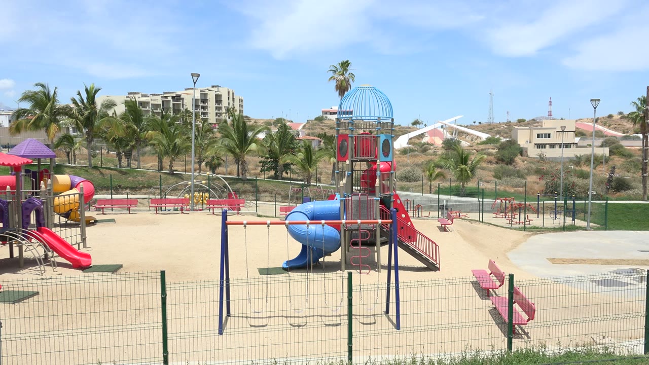 Los Cabos playground frame centered on a tall play tower with a blue dome, red stairs, blue tube slide, swing set, benches, and no visible people.
