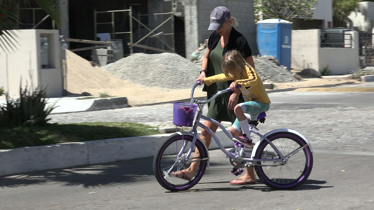 Woman walking beside a child on a purple bicycle.