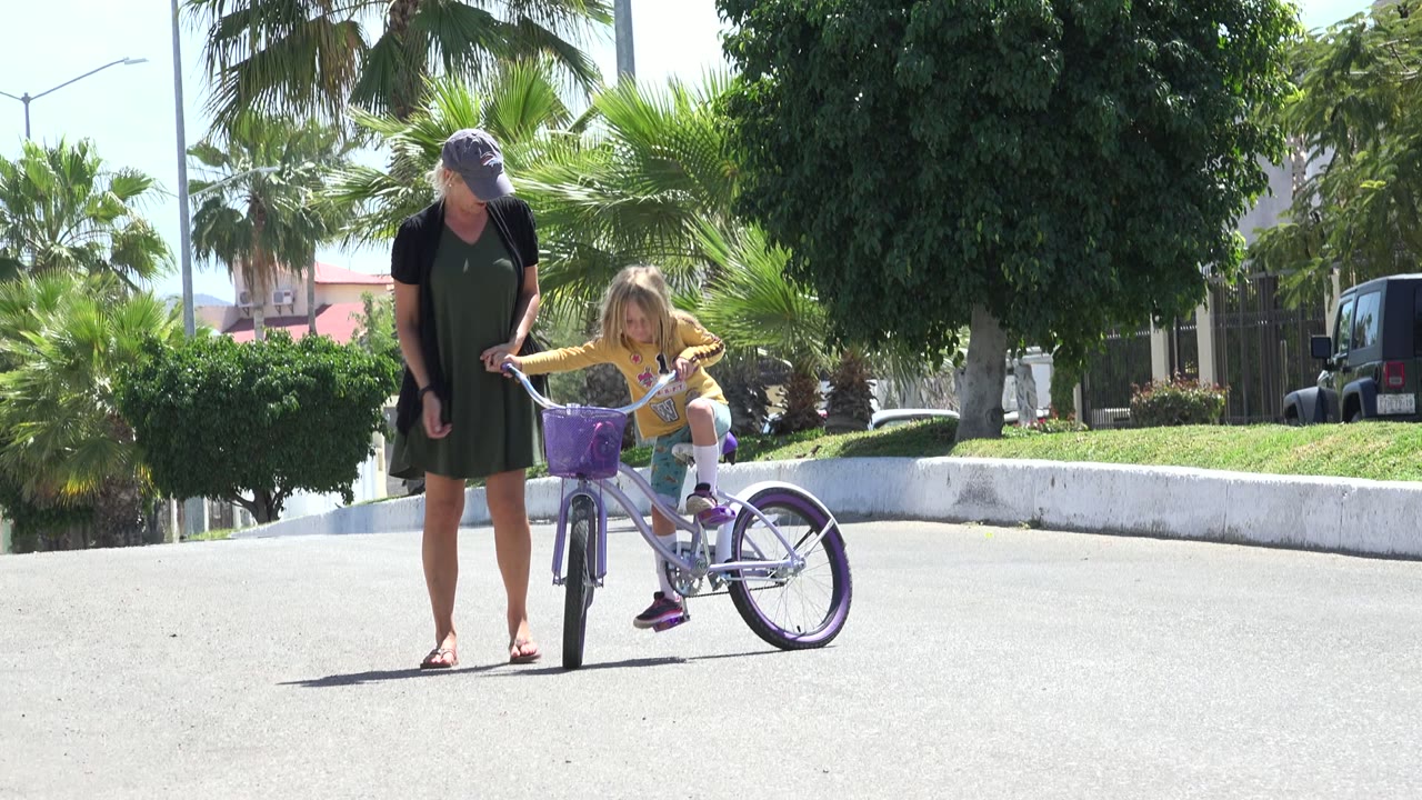 Woman holding a young girl's bicycle on a sunny street.