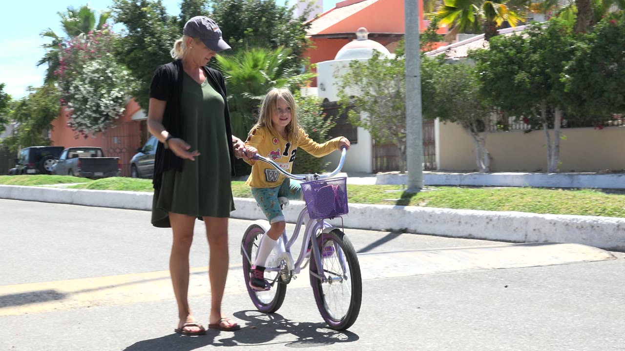 Mother standing beside young girl on a small bicycle
