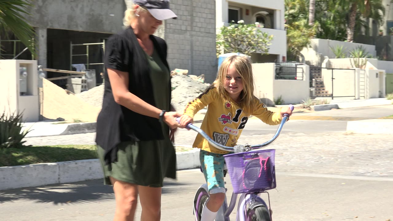 Adult woman walking beside a young girl on a purple bicycle