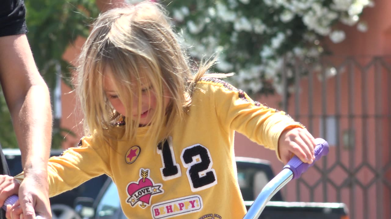 Young girl in a yellow shirt holding bicycle handlebars outdoors.