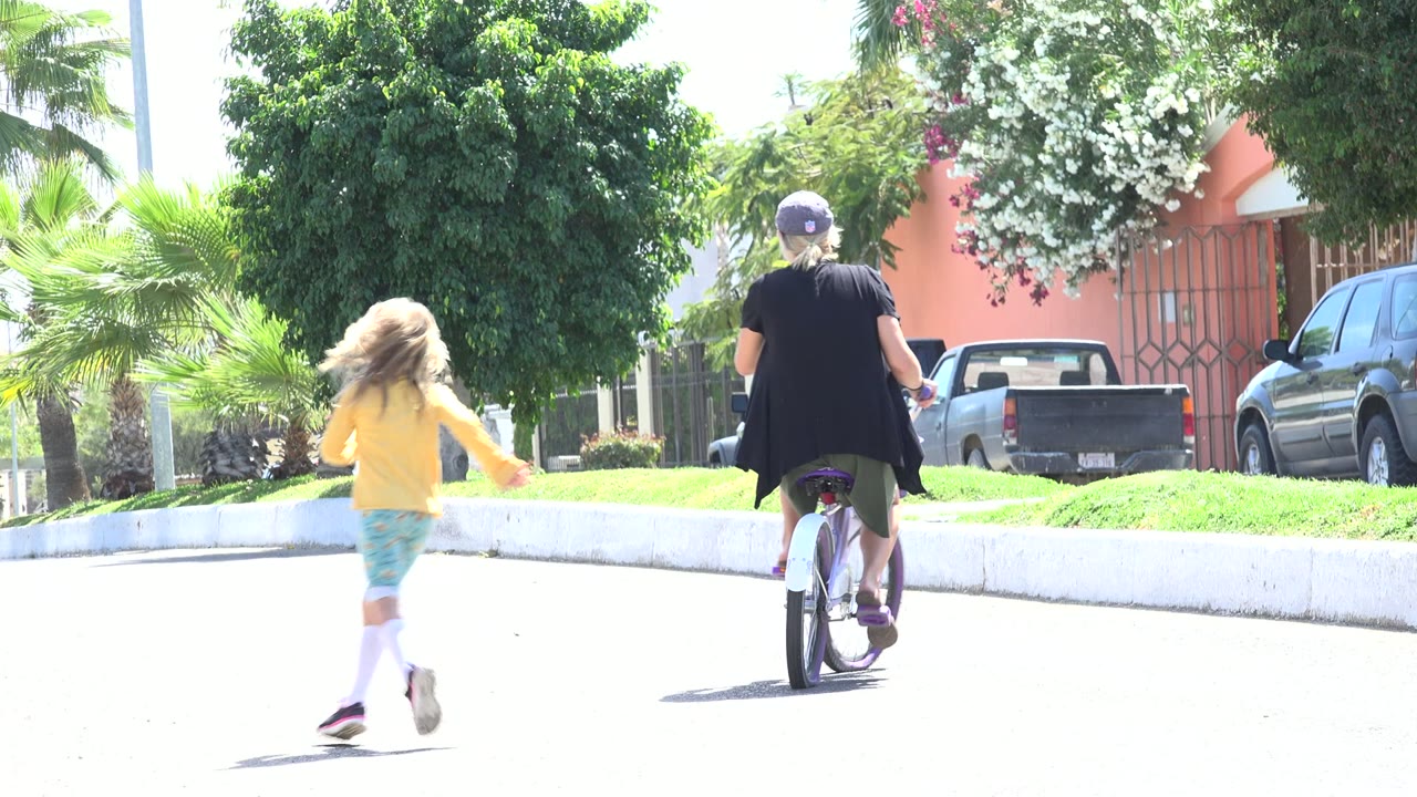 Young girl runs toward an adult on a bicycle on a sunny street.