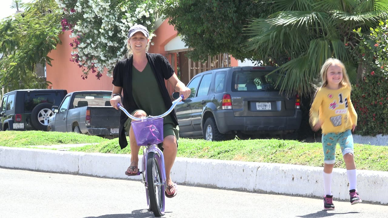 Woman on a purple bicycle with a child running beside a residential street.