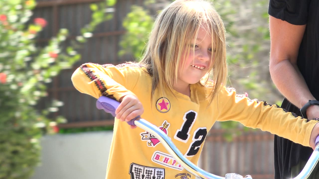 Young child holding purple bicycle handlebars with an adult partly visible beside her.