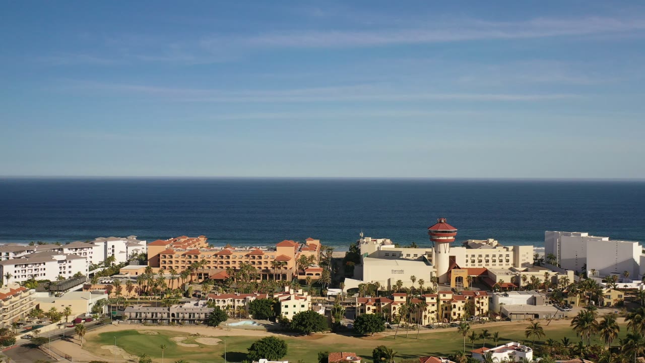 Aerial view of coastal buildings, golf course, beach, and ocean under clear sky.