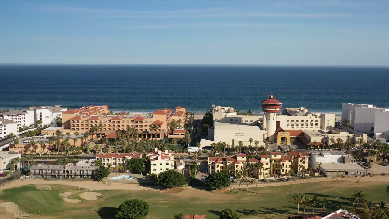 Aerial view of coastal buildings, golf course, and ocean horizon