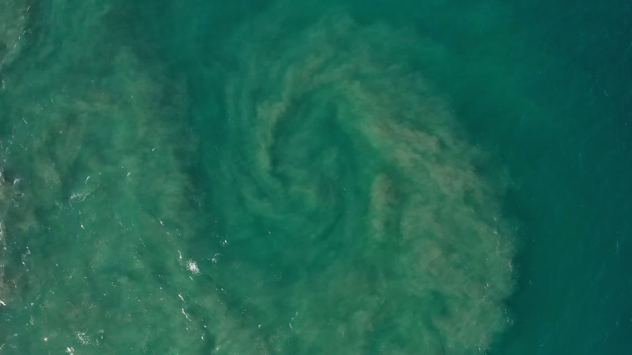 Green seawater with pale sand swirling beneath the surface.