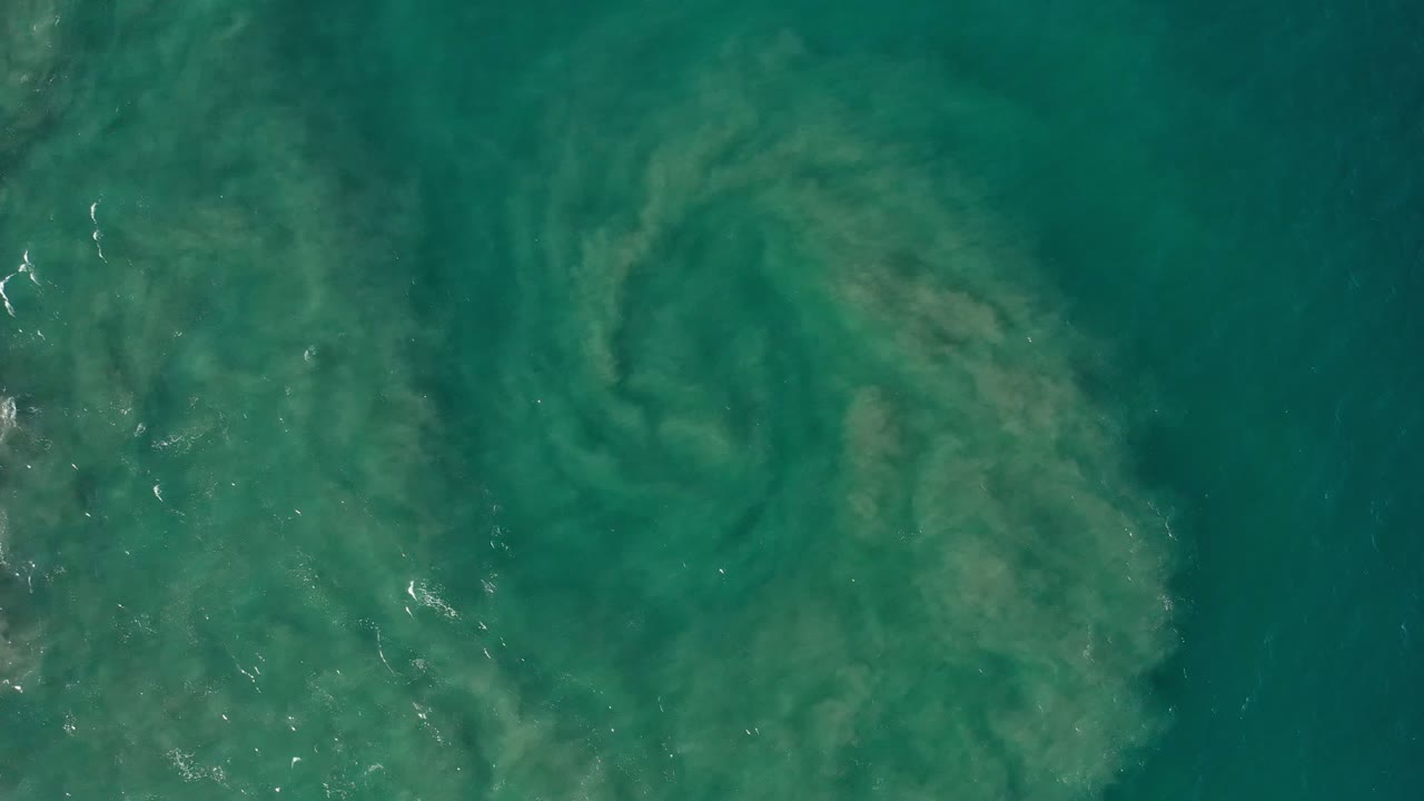 Green ocean water in Los Cabos, Mexico, with a cloudy pale sand plume centered below the surface and no visible people.