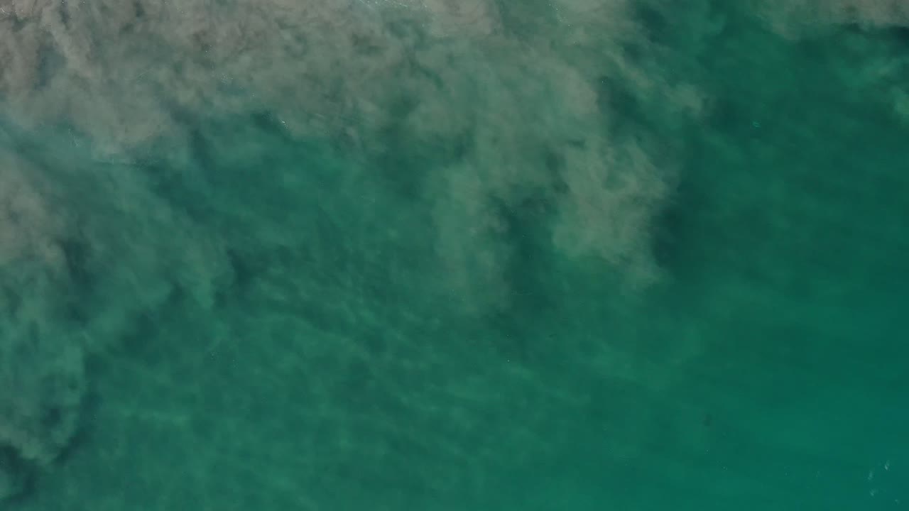 Aerial view of teal ocean water and dark submerged coastline patches