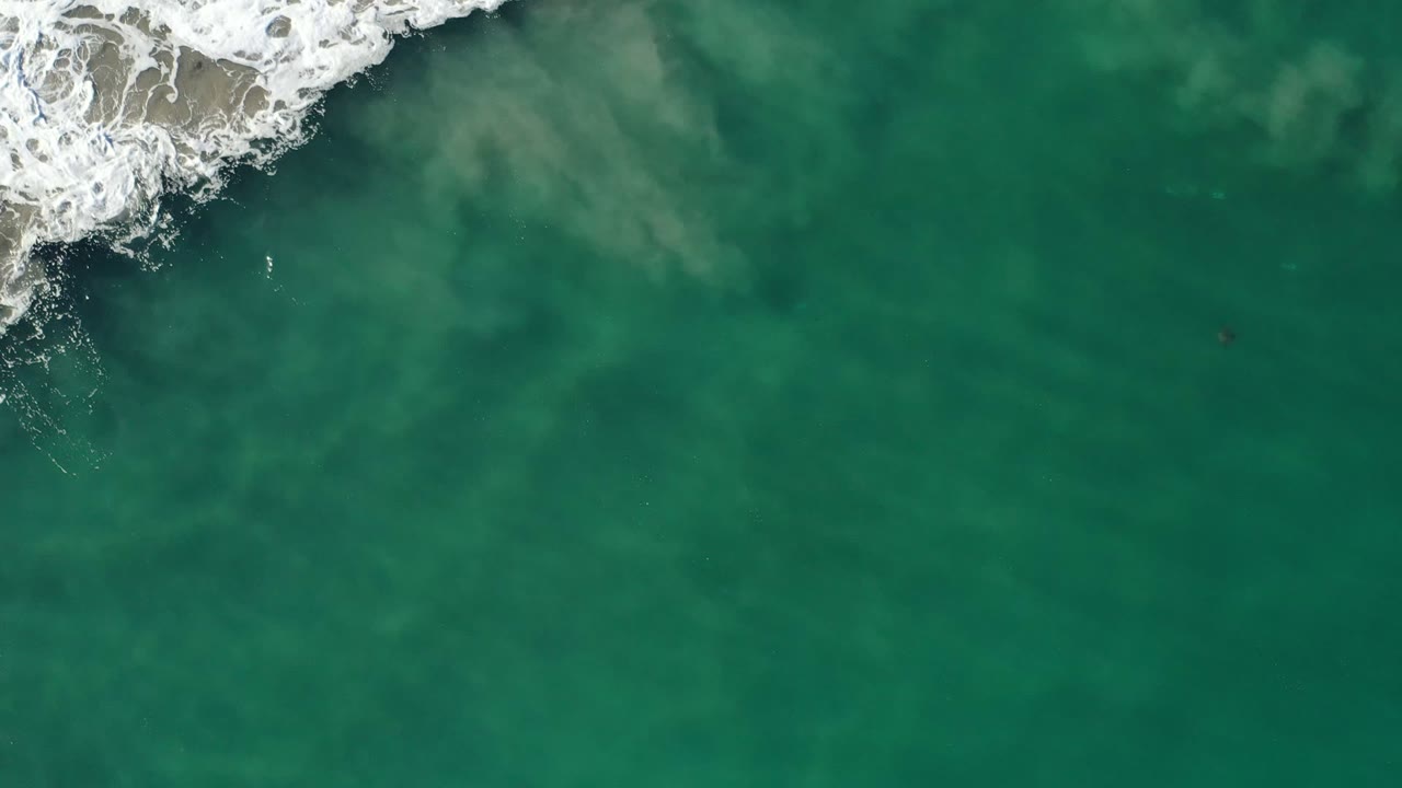 White surf over green ocean water from above.