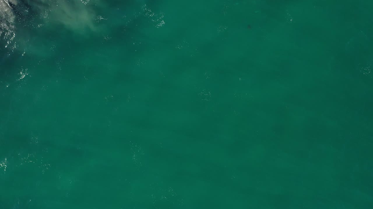 Green ocean water with faint sand clouds and small surf foam at the corners.