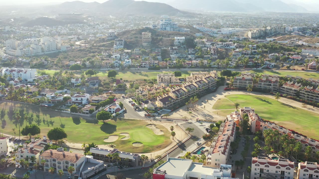 Aerial view of homes, roads, golf greens, and hills.