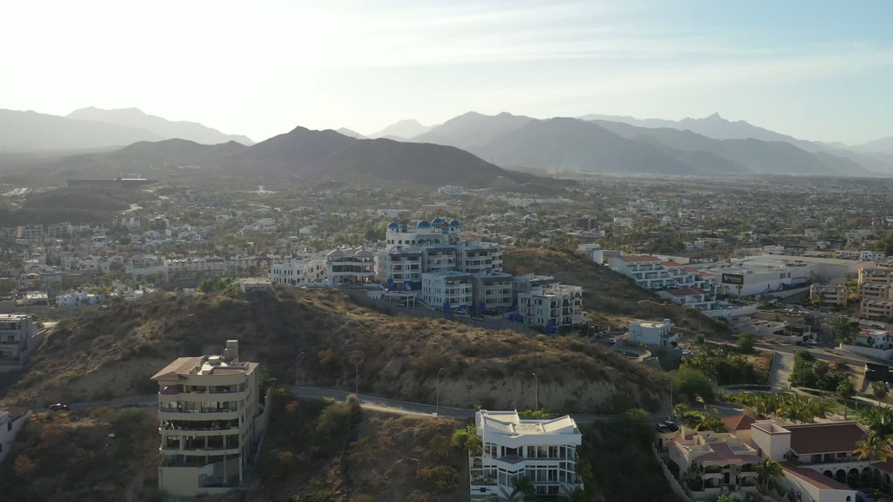 Aerial view of hillside buildings, city blocks, and distant mountains.