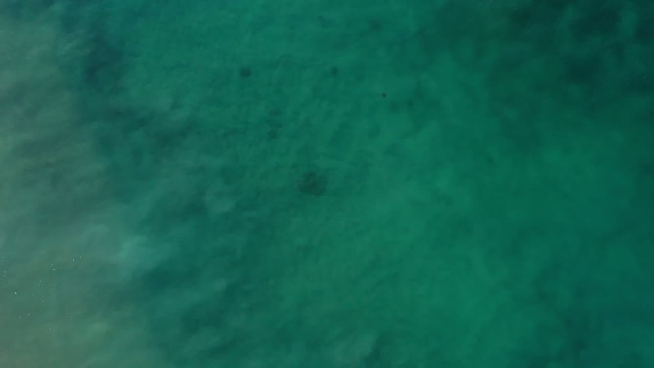 Aerial frame of turquoise green ocean in Los Cabos, Mexico, with subtle cloudlike tonal variation across the water and no visible people.
