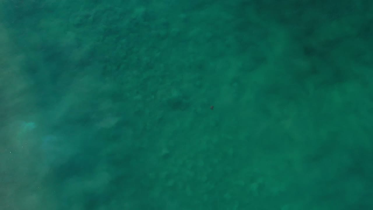 Overhead view of teal-green seawater in Los Cabos, Mexico, with soft dark patches below the surface and no visible people.