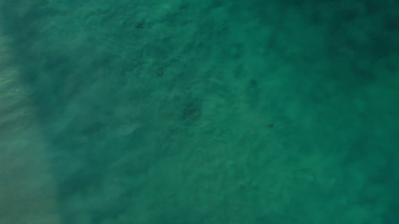 Top-down view of teal ocean water near Los Cabos, Mexico, with faint surface ripples, shadowy underwater areas, and no visible people.