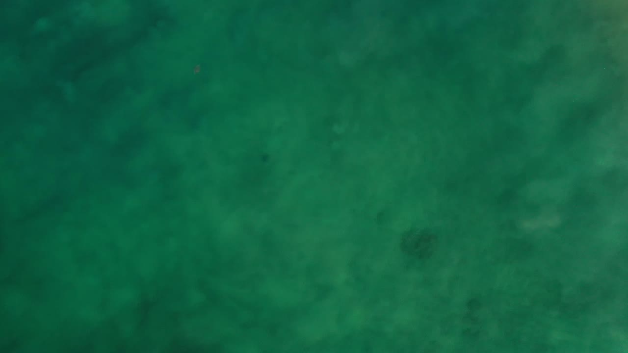Top-down view of shallow green ocean in Los Cabos, Mexico, with mottled water color and no visible people or shoreline.