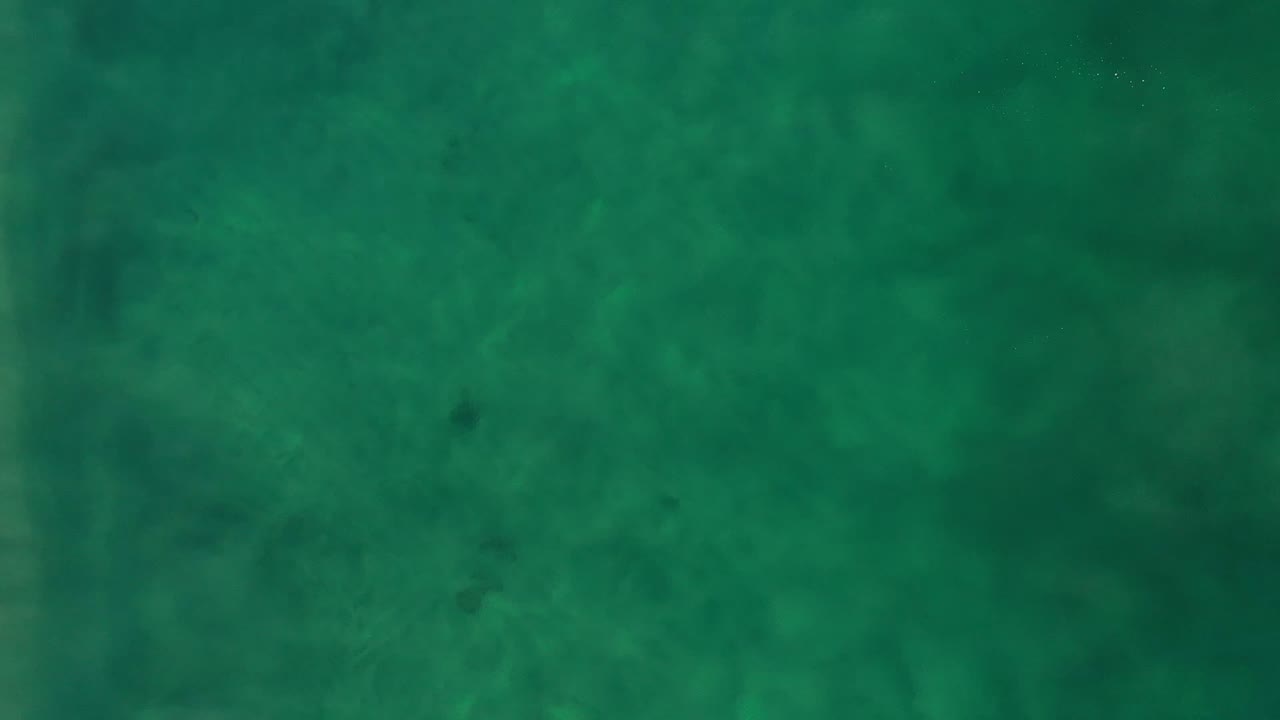Aerial view over Los Cabos green ocean water, with the frame filled by soft surface texture and no visible people.