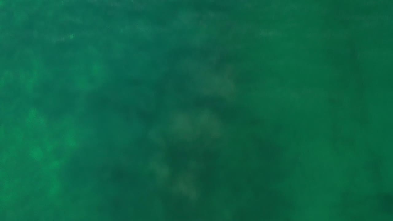 Overhead view of blue-green ocean water in Los Cabos, Mexico, with soft darker patches below the surface and no visible people.