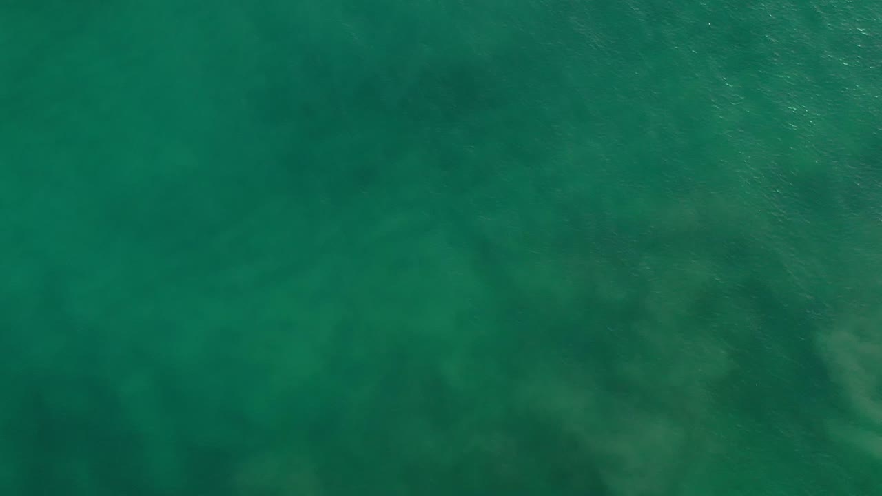 Overhead turquoise water in Los Cabos, Mexico, showing mottled darker areas beneath the surface and no visible people.
