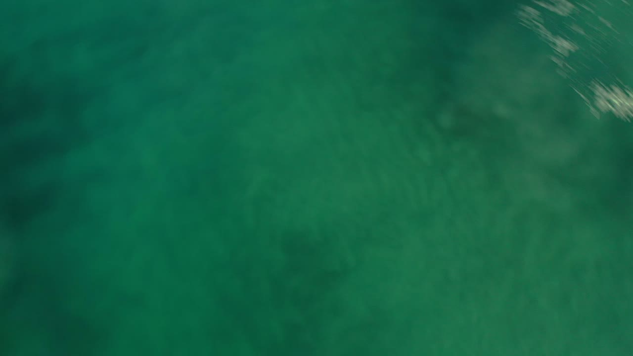 Overhead view of green-blue ocean water with darker patches.