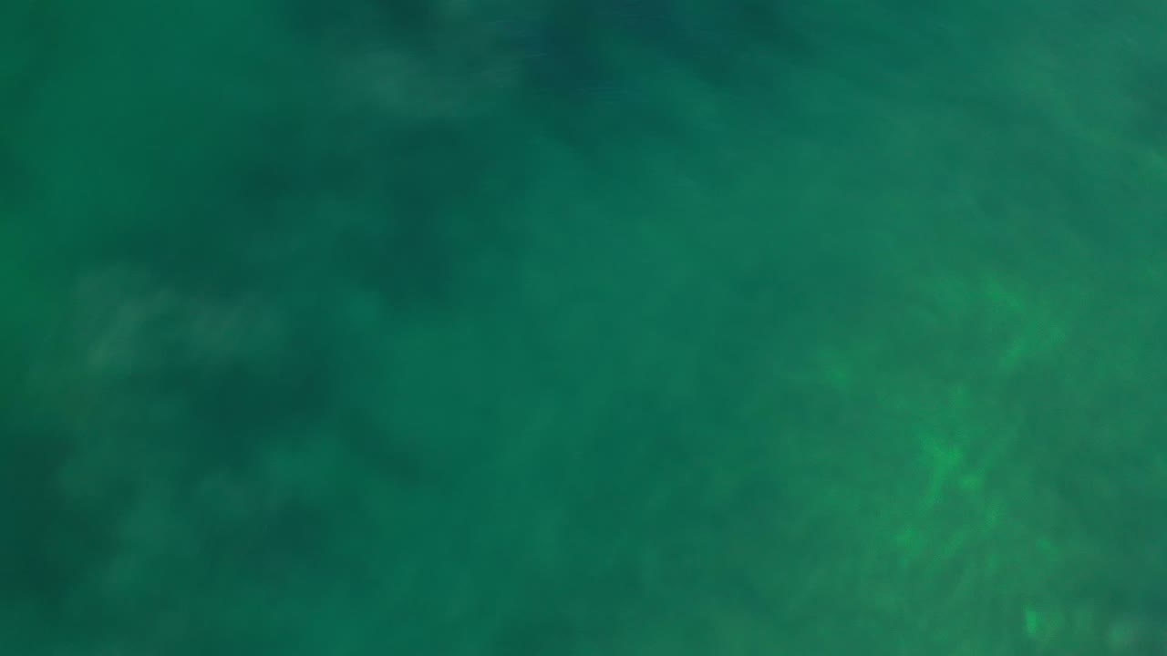 Clear green ocean surface in Los Cabos, Mexico, with a small sun glint near the upper part of the frame and no visible people.