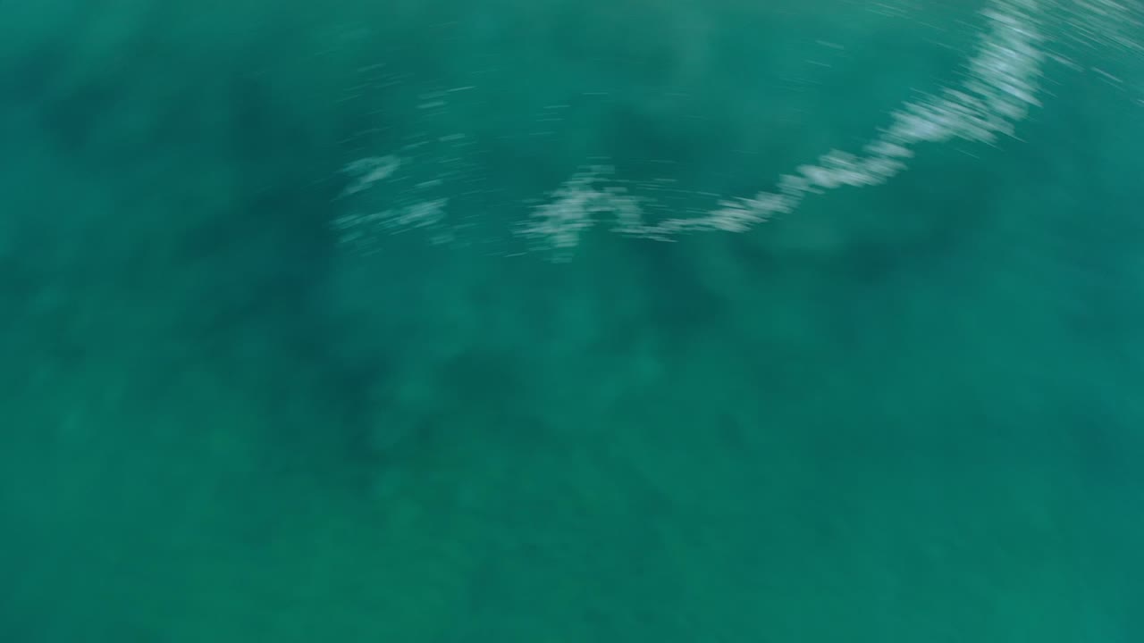Overhead view of clear teal ocean water in Los Cabos, Mexico, with dark reef patches below the surface and no visible people.