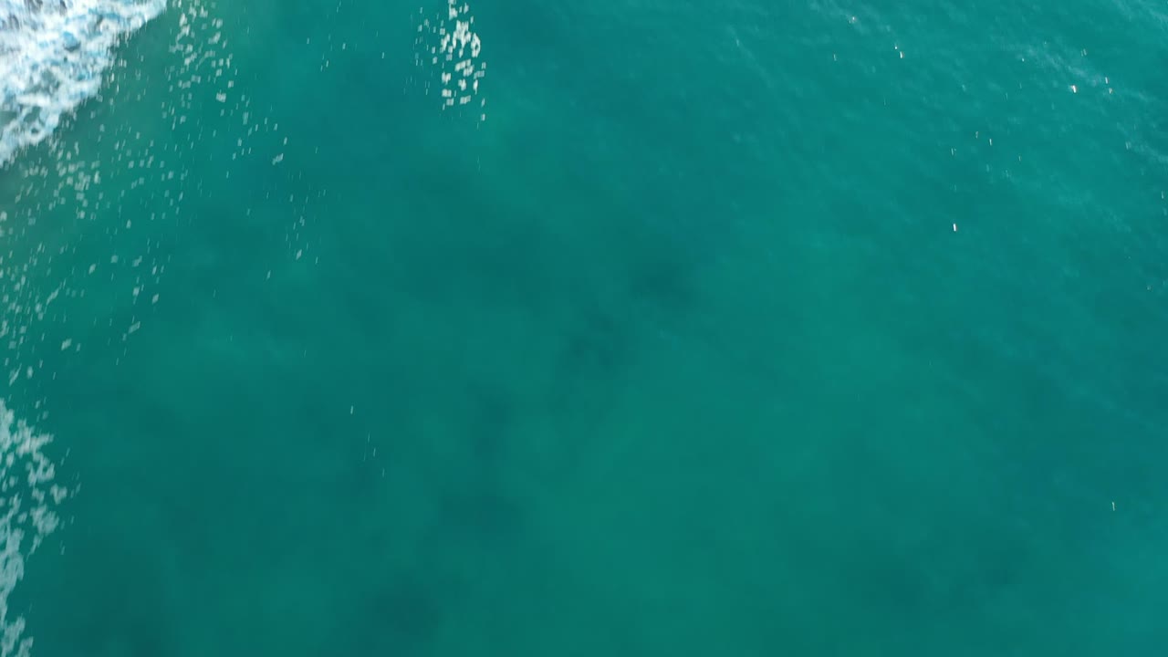 Overhead view of turquoise water in Los Cabos, Mexico, with white surf just entering at the upper left and no visible people.