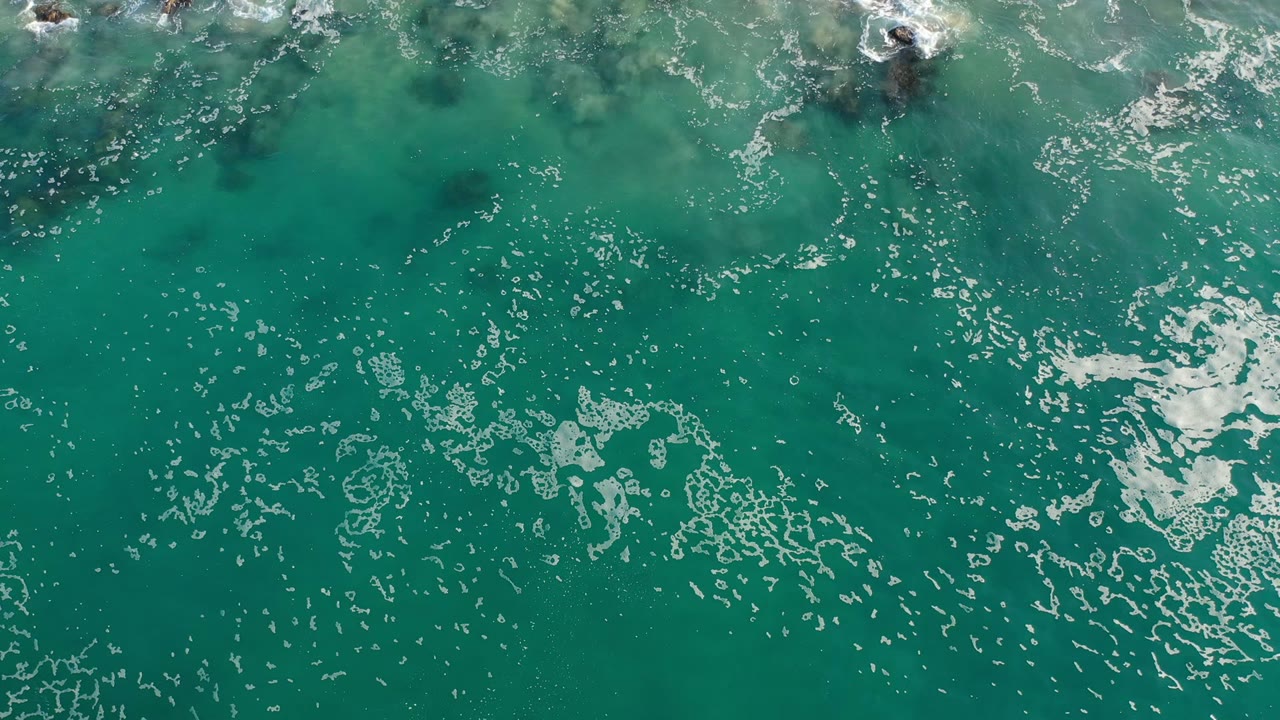 Overhead turquoise seawater with foam and dark rocks near the top edge.