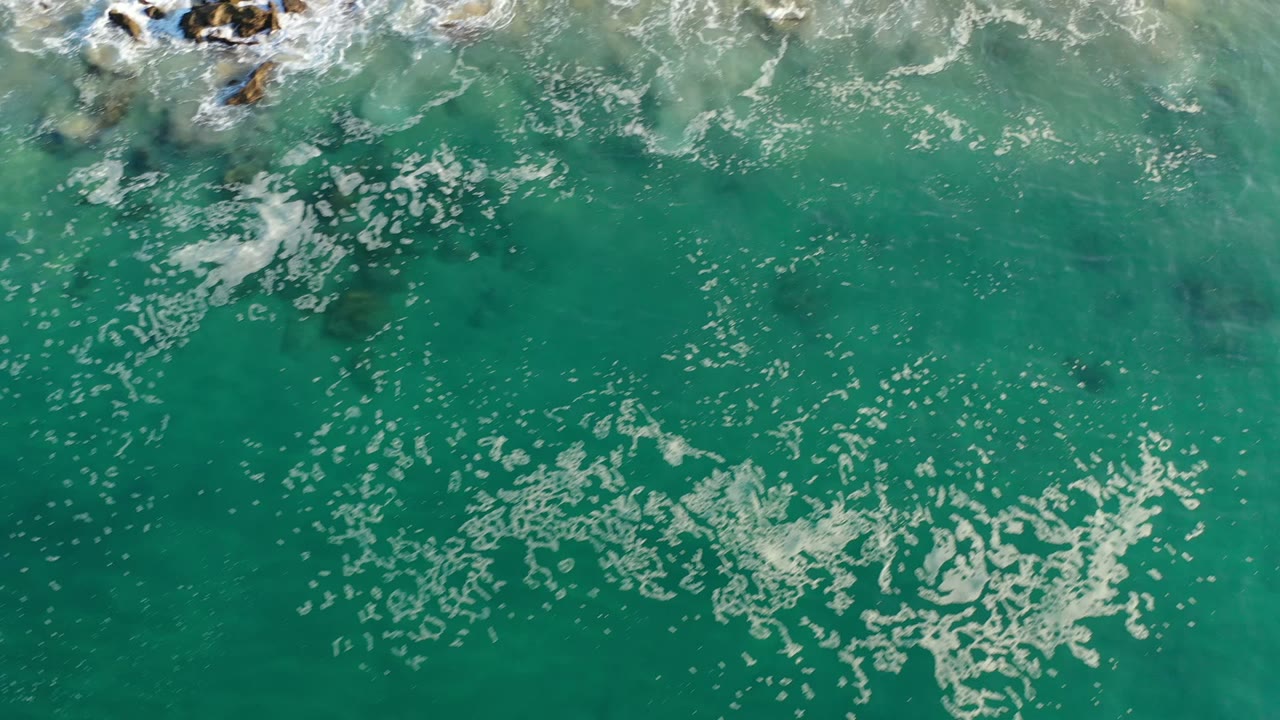 Turquoise ocean water with foam and rocks near the top edge.
