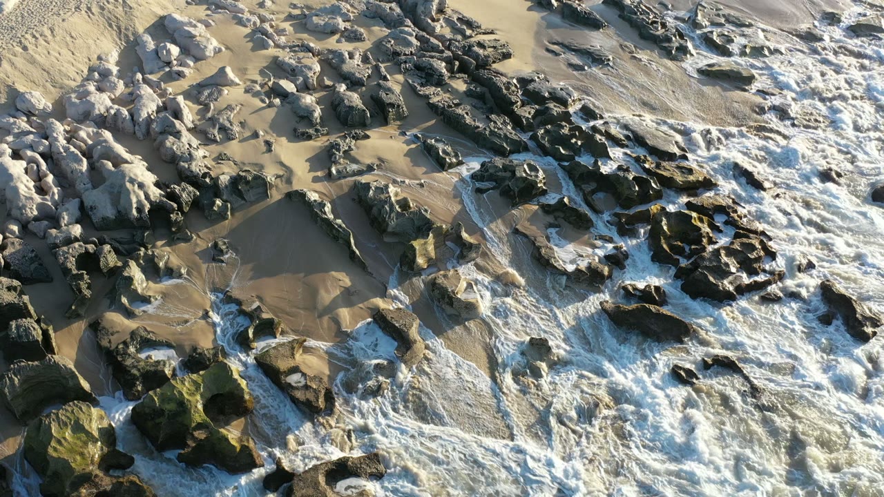 Overhead surf and dark rocks on wet sand.