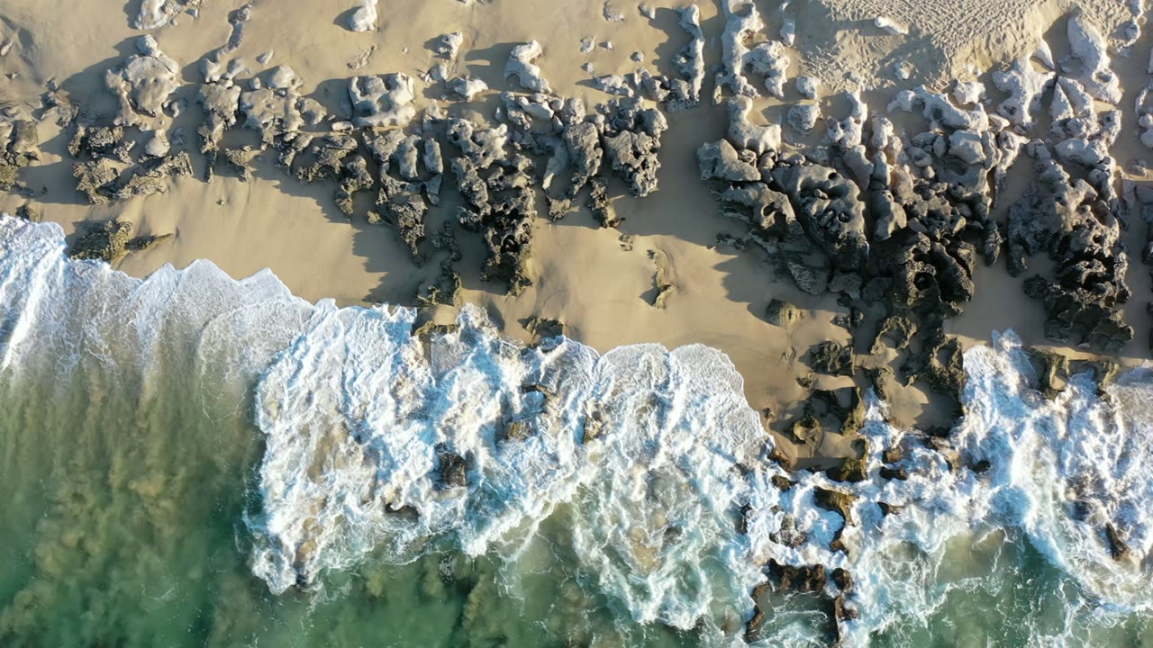 Overhead surf washing onto a rocky sandy shoreline.