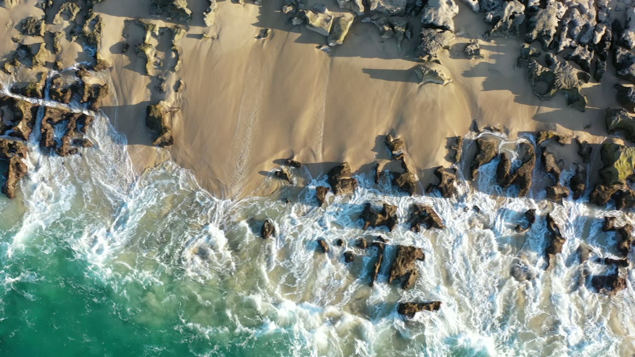 Overhead surf washing around rocks on a sandy beach