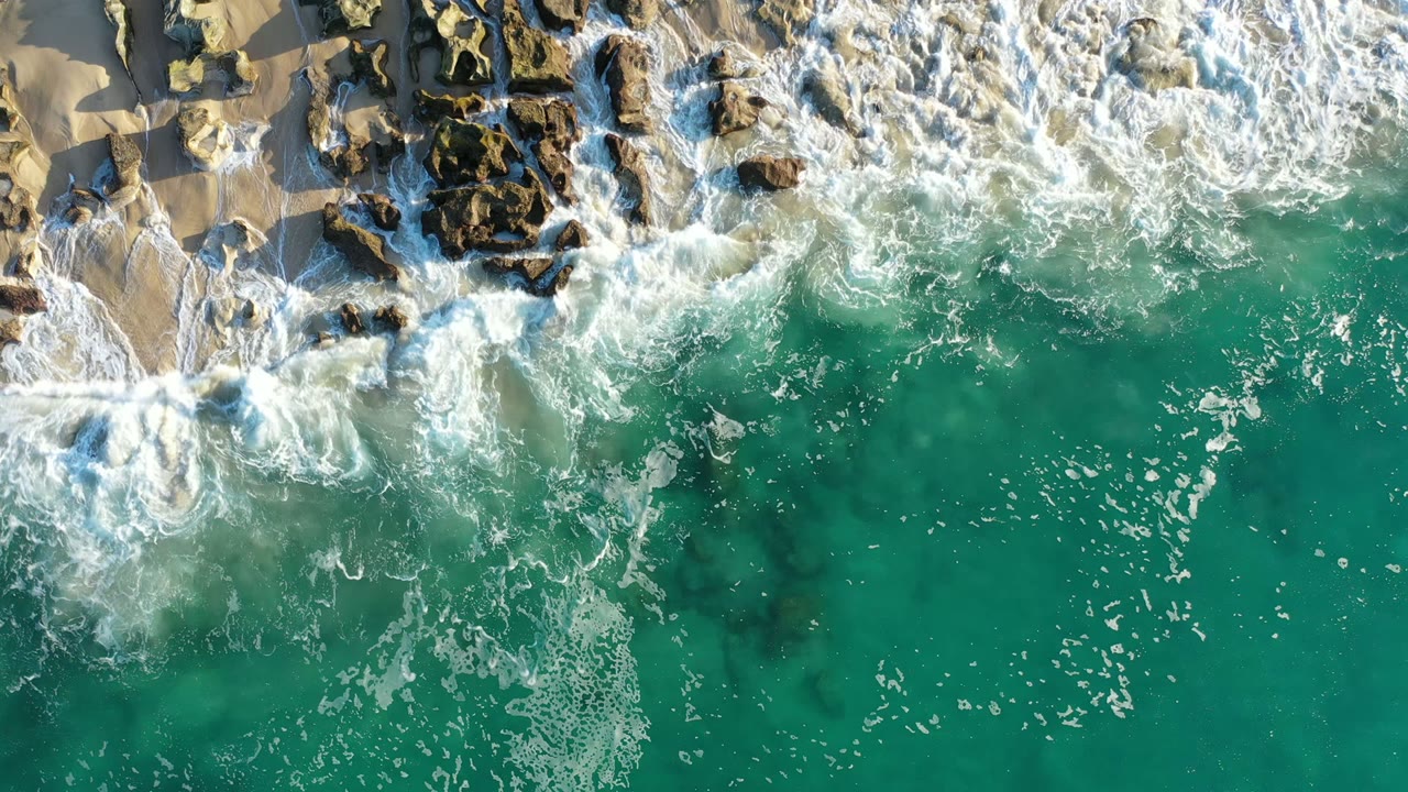 Overhead surf washing across rocks and turquoise water
