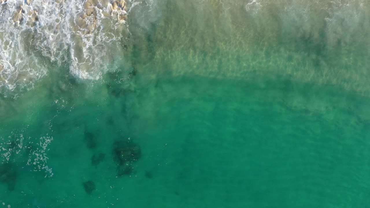 Overhead turquoise water and foamy waves meeting sand.