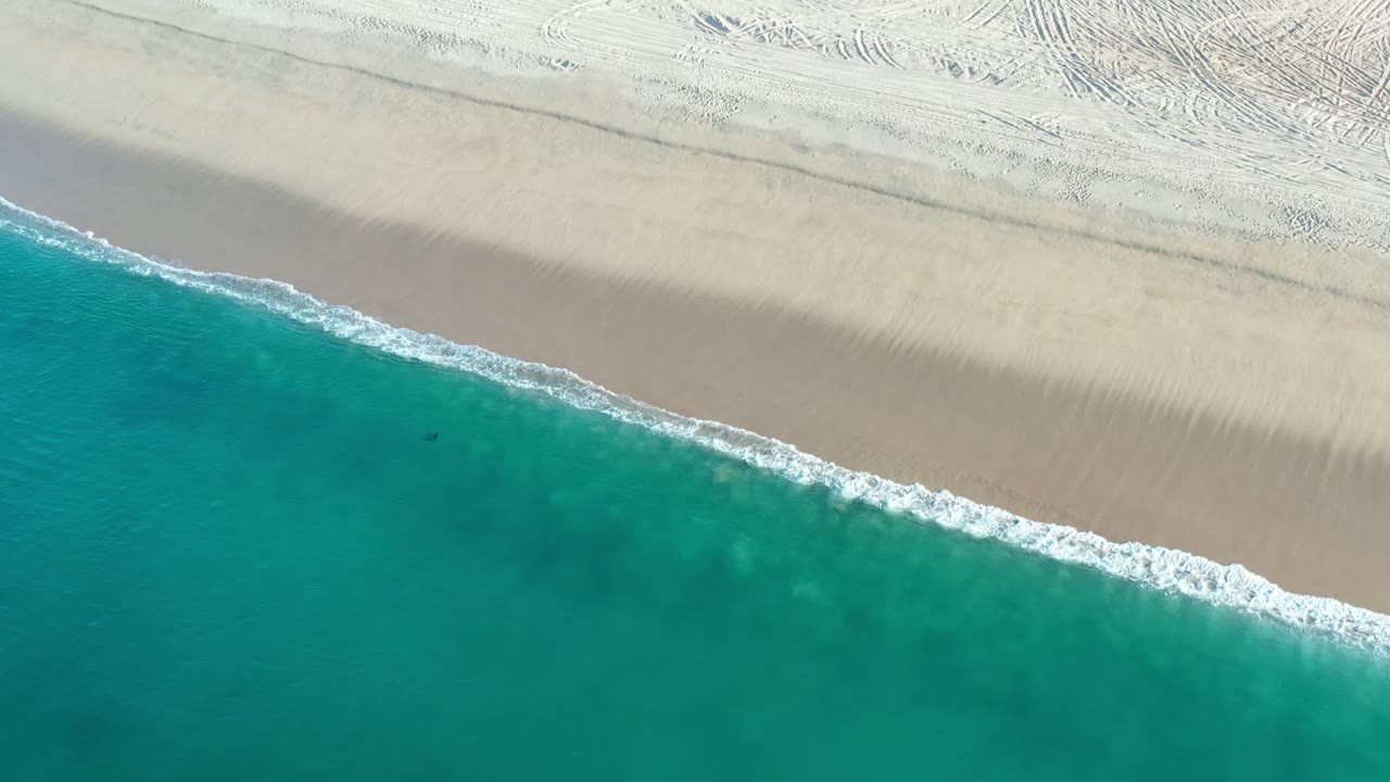 Overhead view of turquoise water meeting pale beach sand.